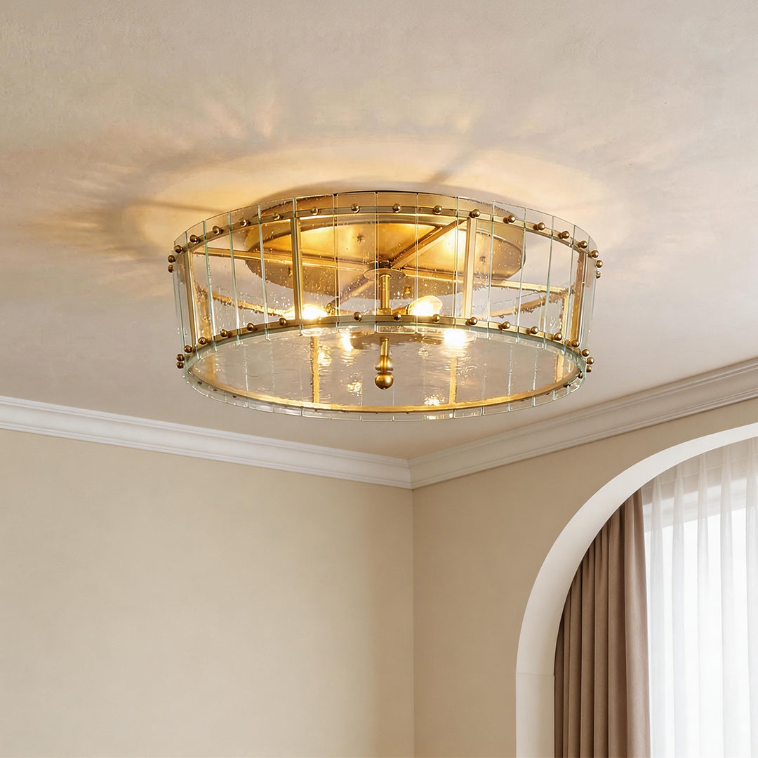 Elegant flush mount gold light with a drum glass shade and a warm glowing brass fixture.