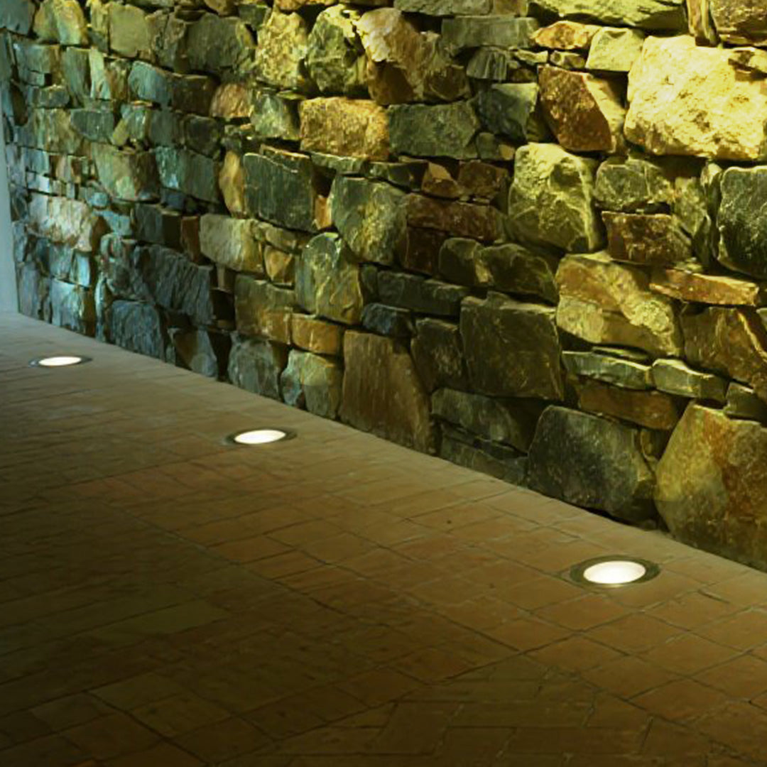 Flush-mounted ground light illuminating natural stone retaining wall with warm accent lighting