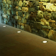 Flush-mounted ground light illuminating natural stone retaining wall with warm accent lighting