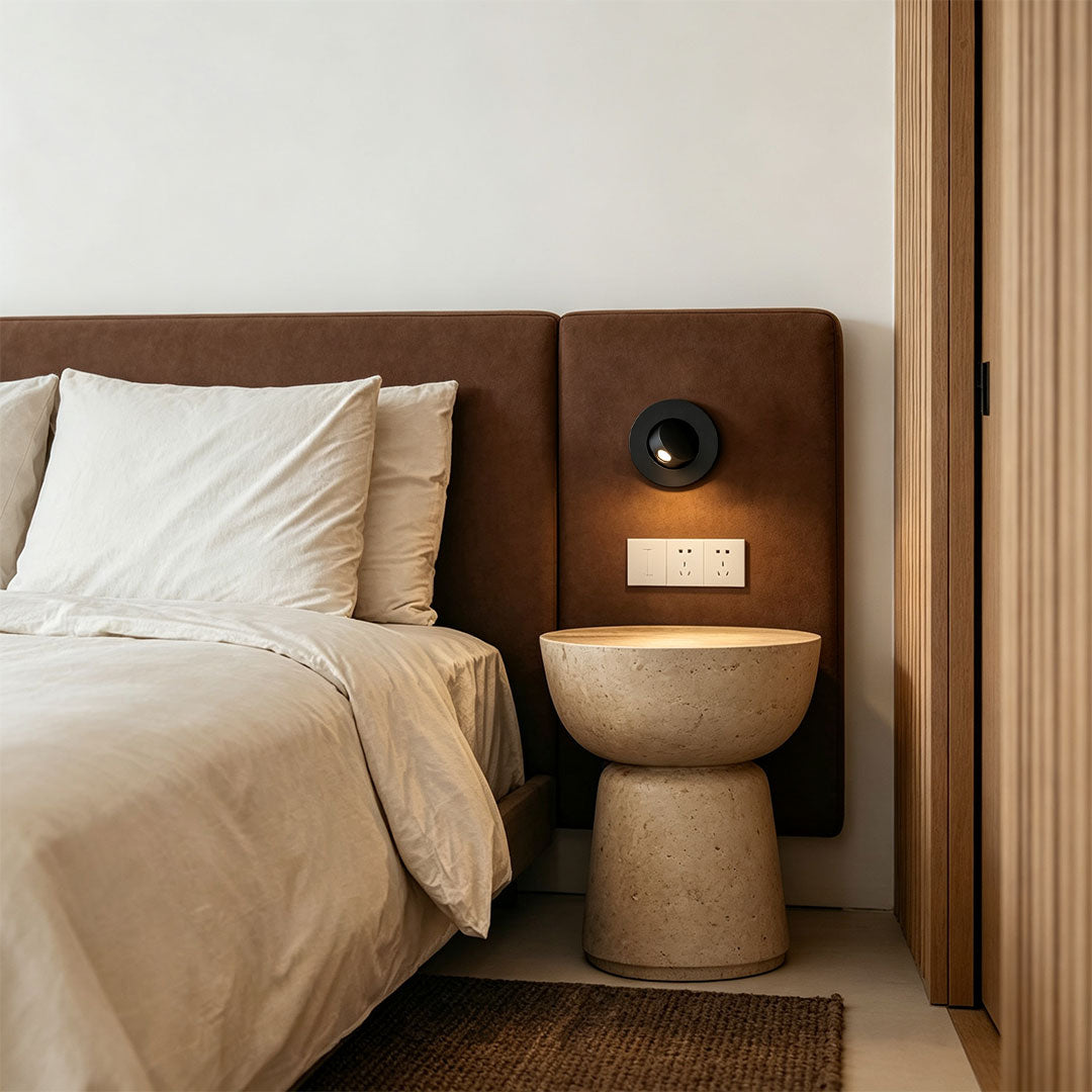 Elegant flush mount wall light beside upholstered bed with minimalist black circular fixture design.