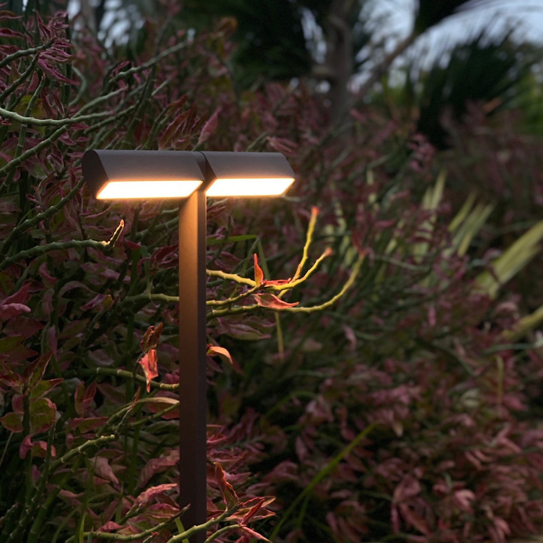 Warm vertical post light highlighting dense garden foliage, offering decorative led pathway lighting at night.