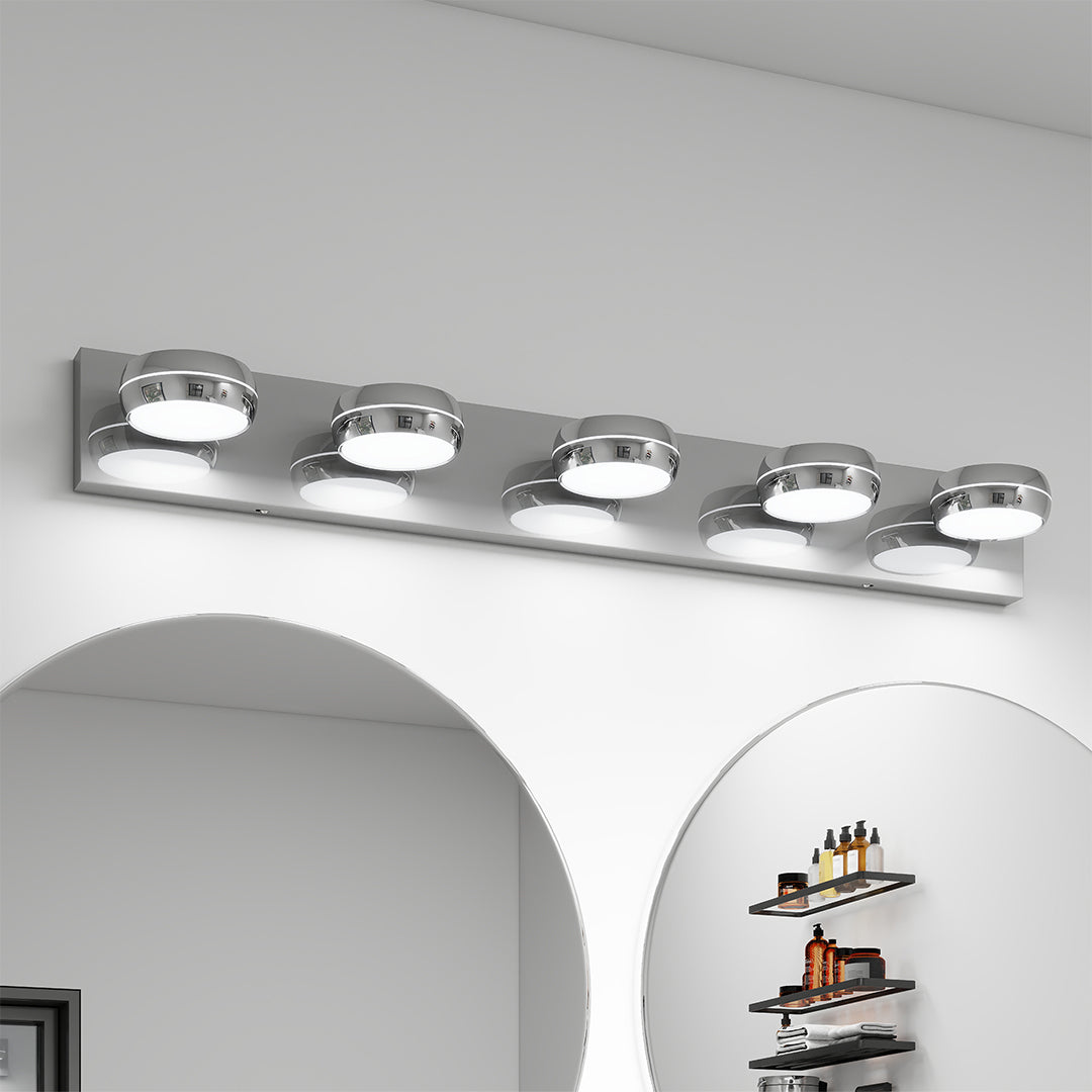 Four-light chrome bathroom vanity light with glass shade chandelier styling installed above round mirror in bright bathroom.