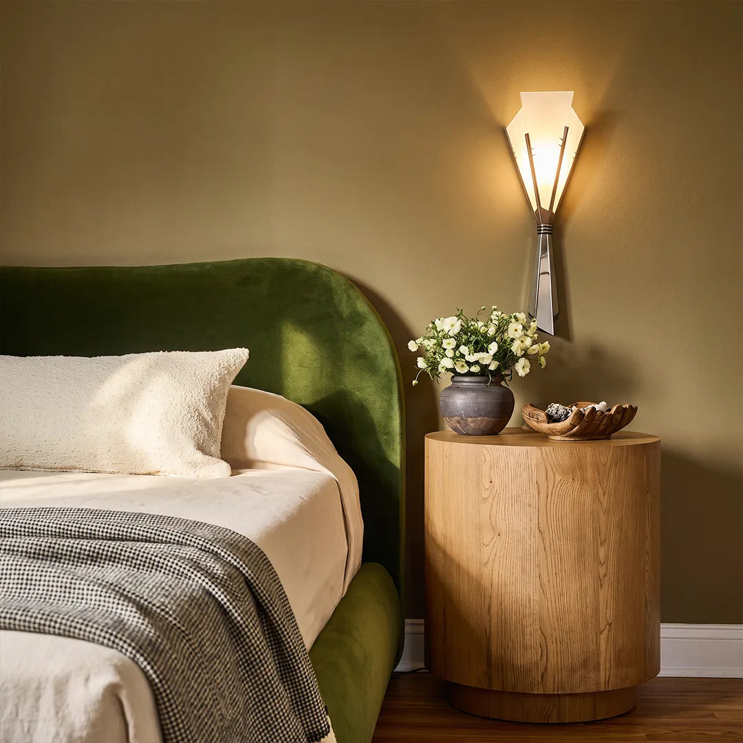 French wall sconces styled beside a bed with a green upholstered headboard and a warm bedside setting.