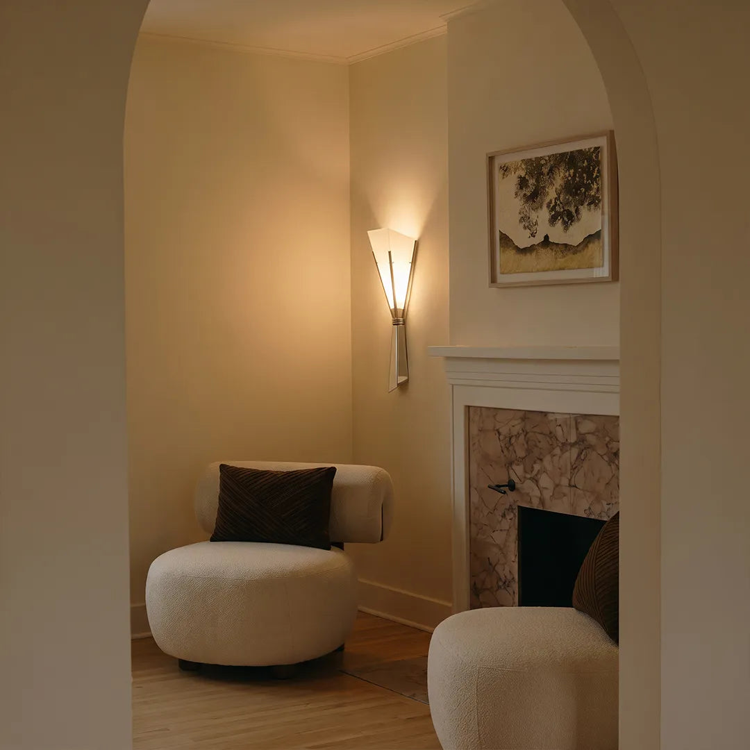 French wall sconces illuminating a cozy reading nook beside a fireplace in a softly lit room.