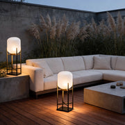 Outdoor standing light with frosted glass shade on wooden deck beside modern sofa at dusk ambiance.