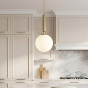 Elegant frosted globe pendant light with a gold stem hanging over a modern marble kitchen island.