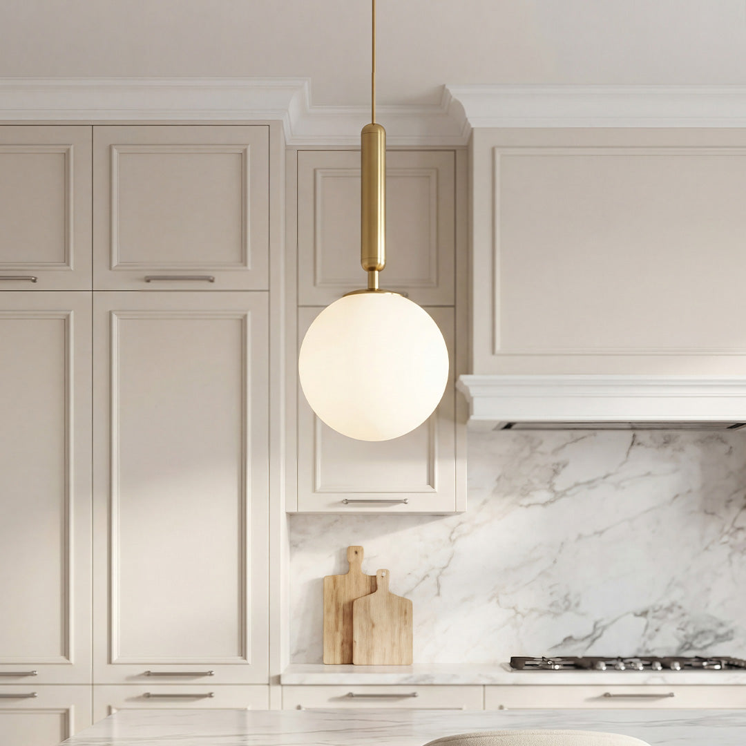 Elegant frosted globe pendant light with a gold stem hanging over a modern marble kitchen island.