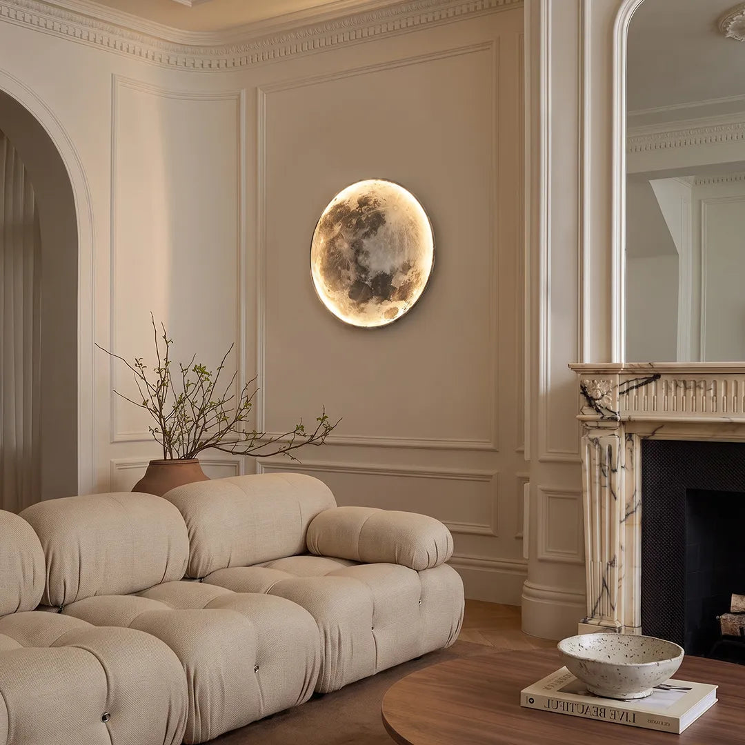 Full moon wall lamp mounted above a curved cream sofa in a refined living room with classic wall molding and a fireplace.