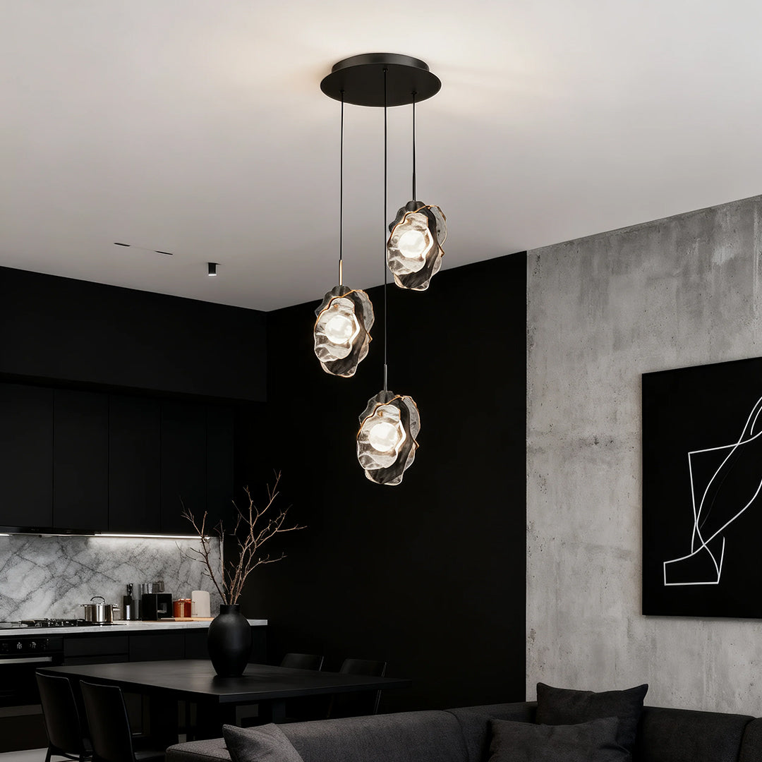 Fun pendant light illuminating modern kitchen with black cabinetry and marble backsplash at dusk