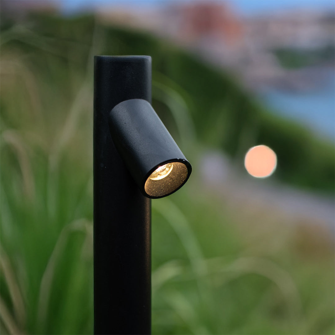 Black LED path light creating warm ambient glow in outdoor garden setting with natural surroundings