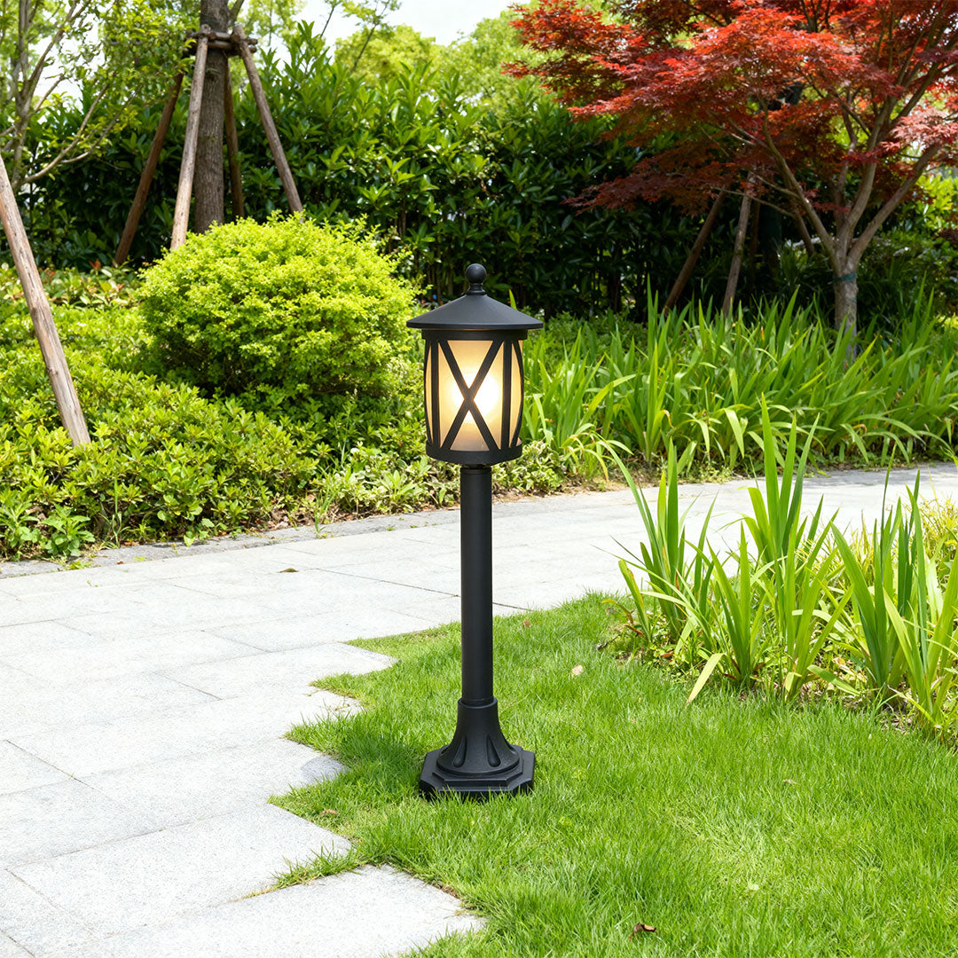Garden bollard light brightening curved pathway edge with lush green shrubs and colorful flower border
