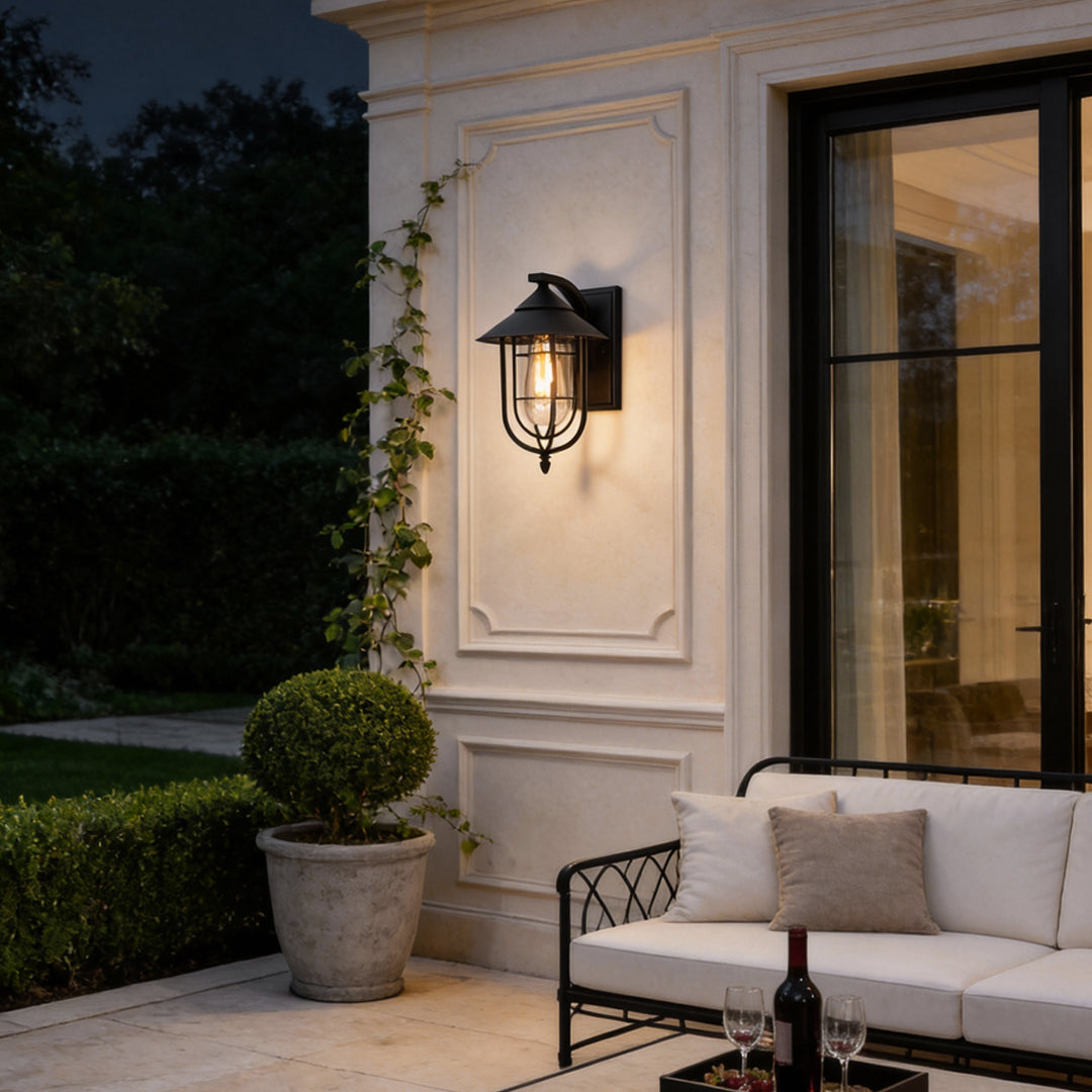 Black metal nautical wall sconce mounted on exterior wall, featuring a cage design and warm filament light.