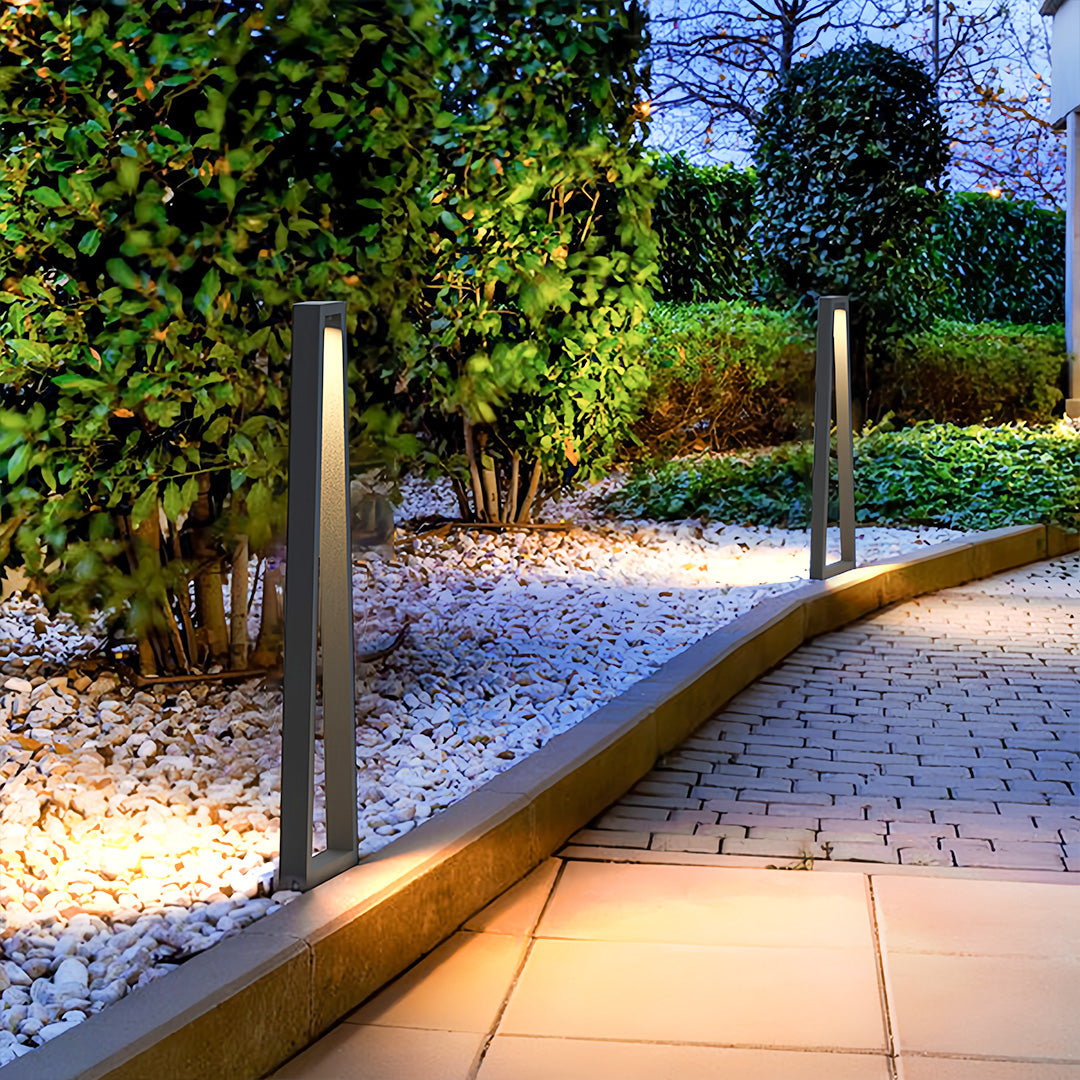 Modern bollards providing outdoor lighting for landscaping along a garden path during early evening.