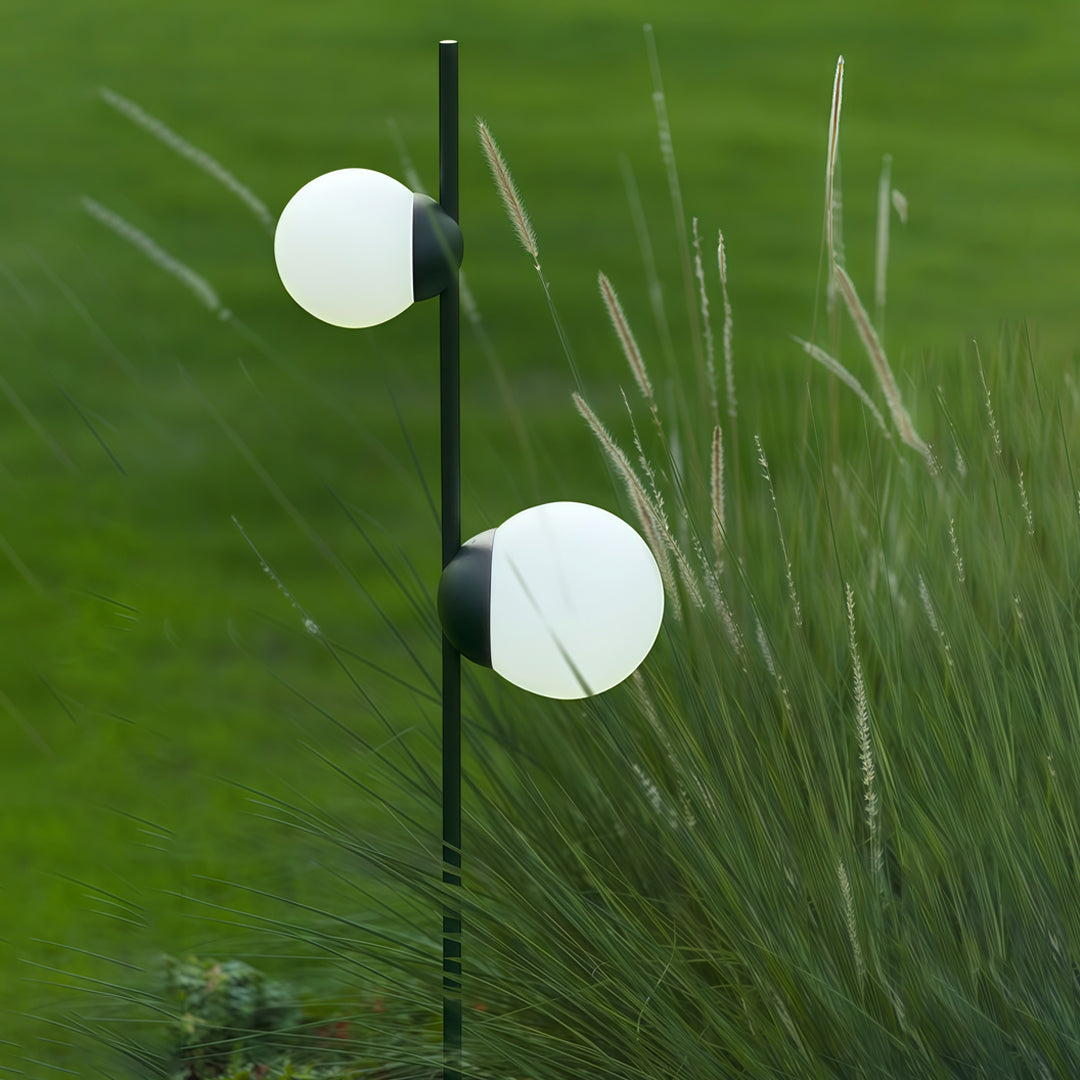 Two glowing spherical garden lamps set in tall grass, creating soft and natural garden pathway lighting in outdoor greenery.