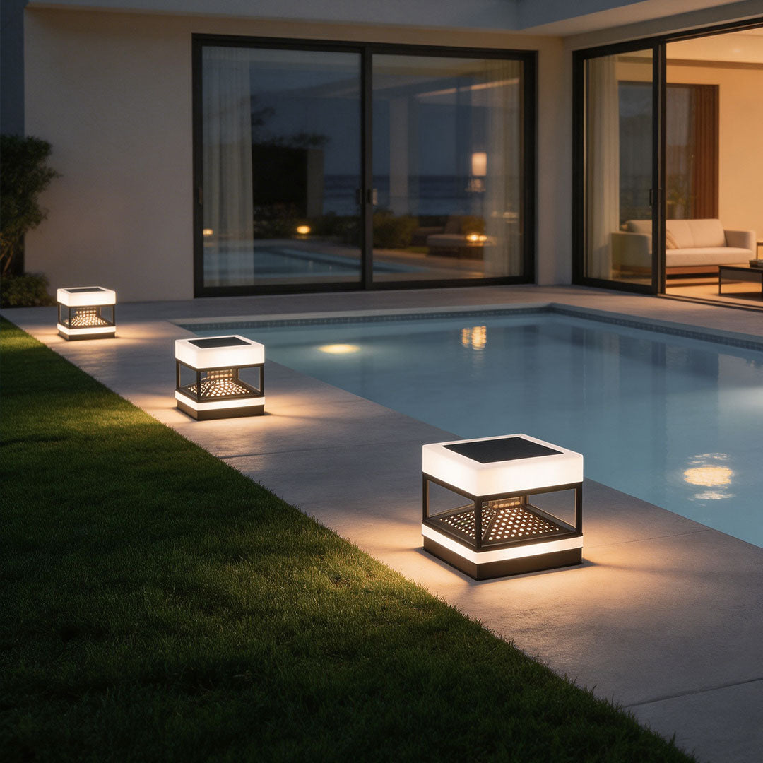 White pillar top lights illuminating the garden pathway near a swimming pool at dusk.