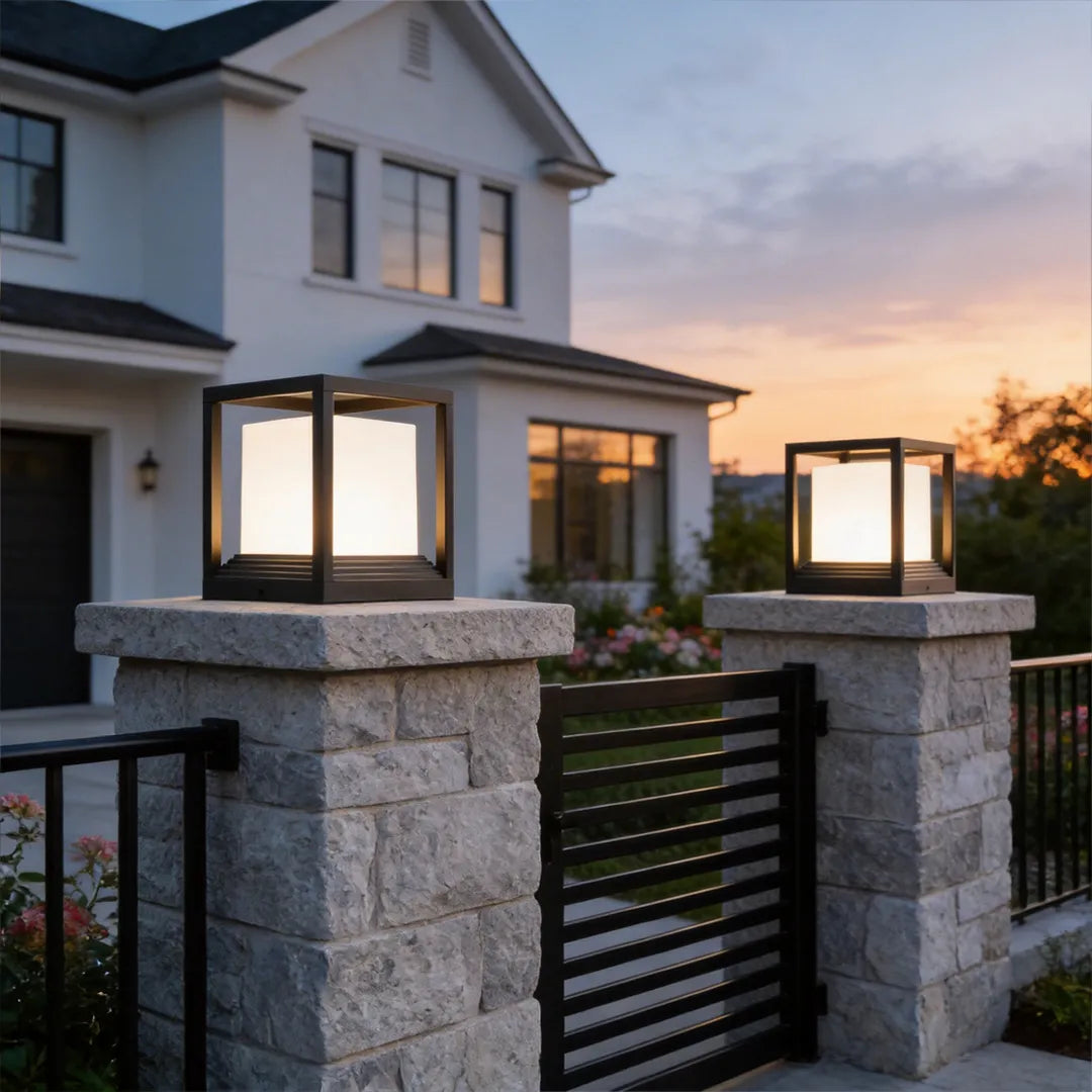 Garden pedestal lights installed on entry gate pillars outside a modern house at dusk.