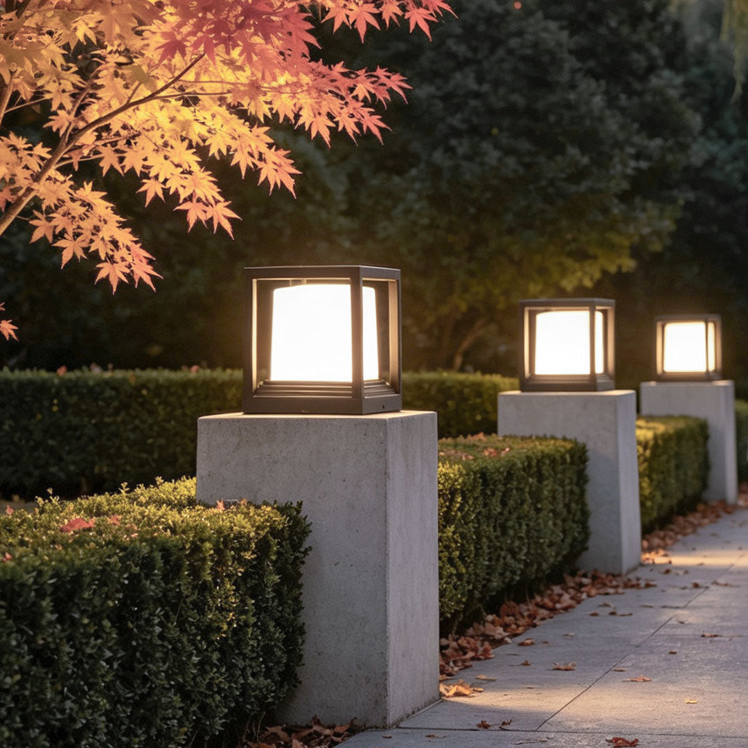 Garden pedestal lights lining a hedge-bordered path with glowing square lantern fixtures.