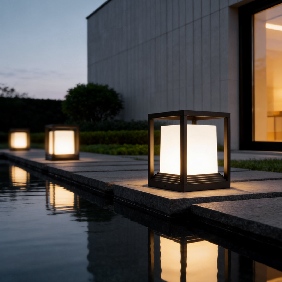 Garden pedestal lights casting warm glow beside infinity pool and modern house.