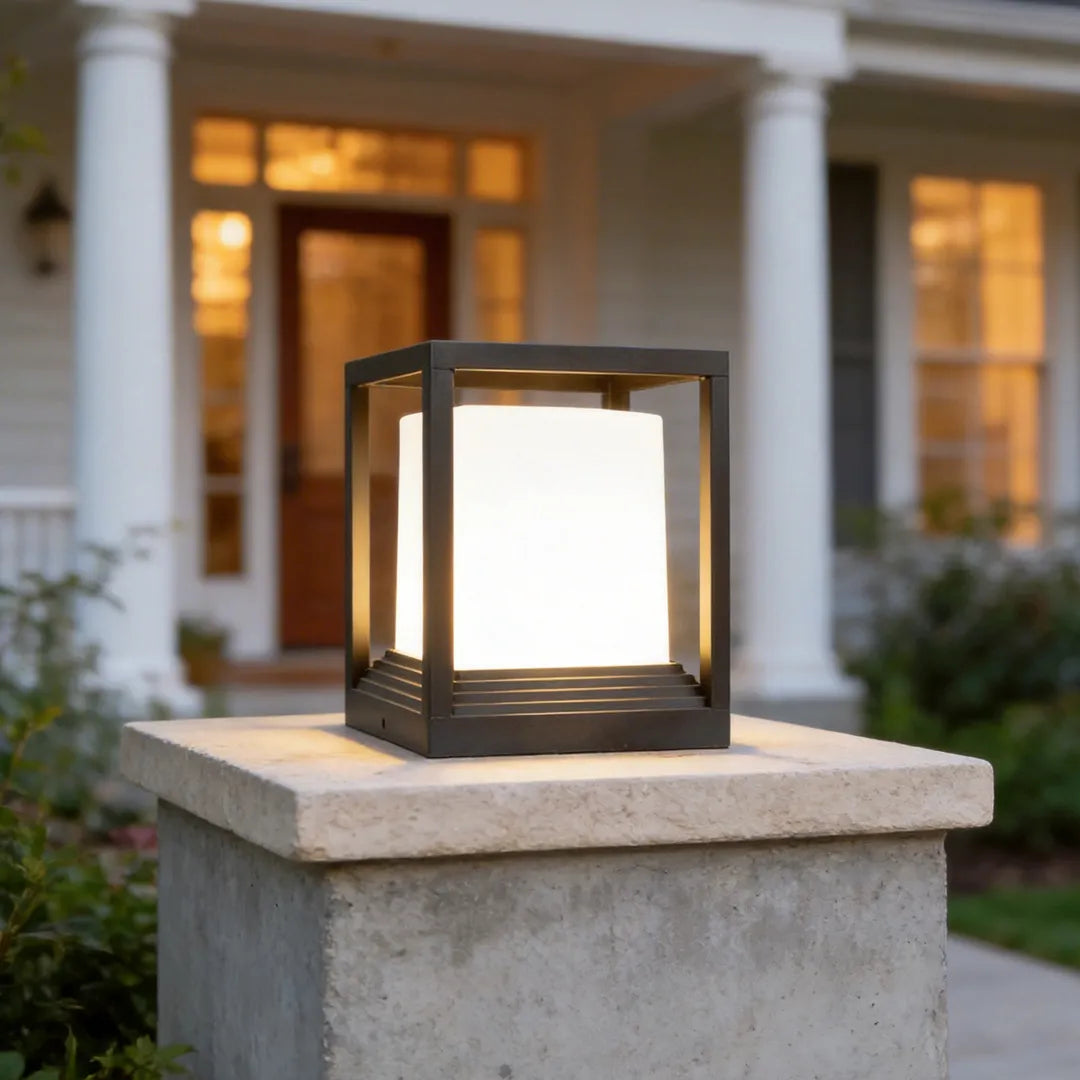 Garden pedestal lights with a modern square lantern design placed on a stone pillar by a front porch.