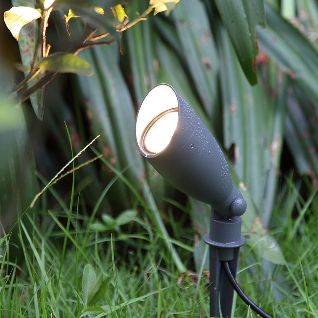 Garden spotlight illuminating tropical plants and foliage with warm LED light in lush landscape setting
