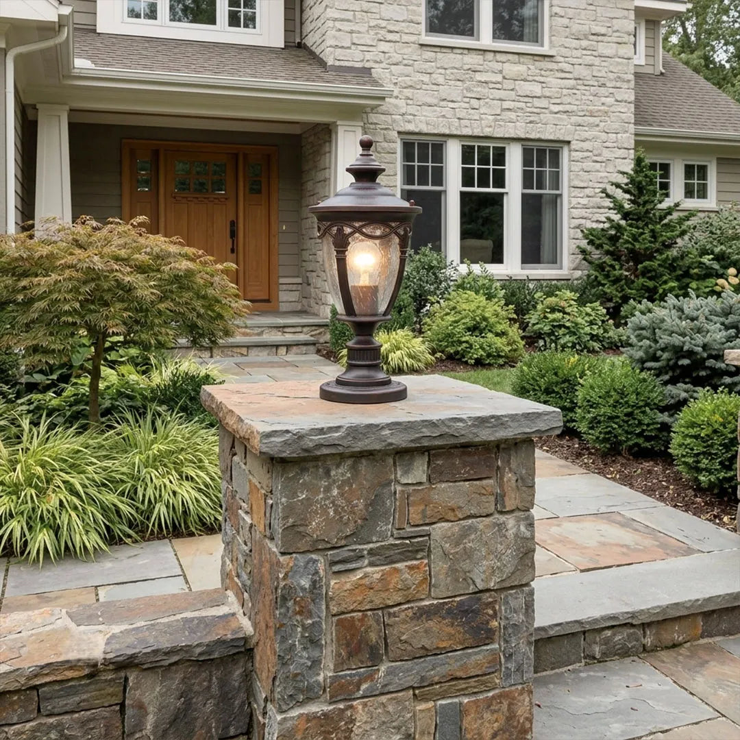 Gate pillar light mounted on a stone entry pillar in front of a landscaped house entrance.