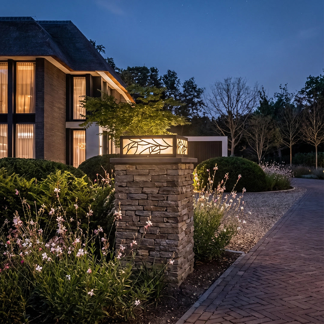 Gate pillar lights mounted on stone columns, illuminating a landscaped driveway entrance at dusk.