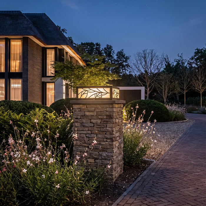 Gate pillar lights mounted on stone columns, illuminating a landscaped driveway entrance at dusk.