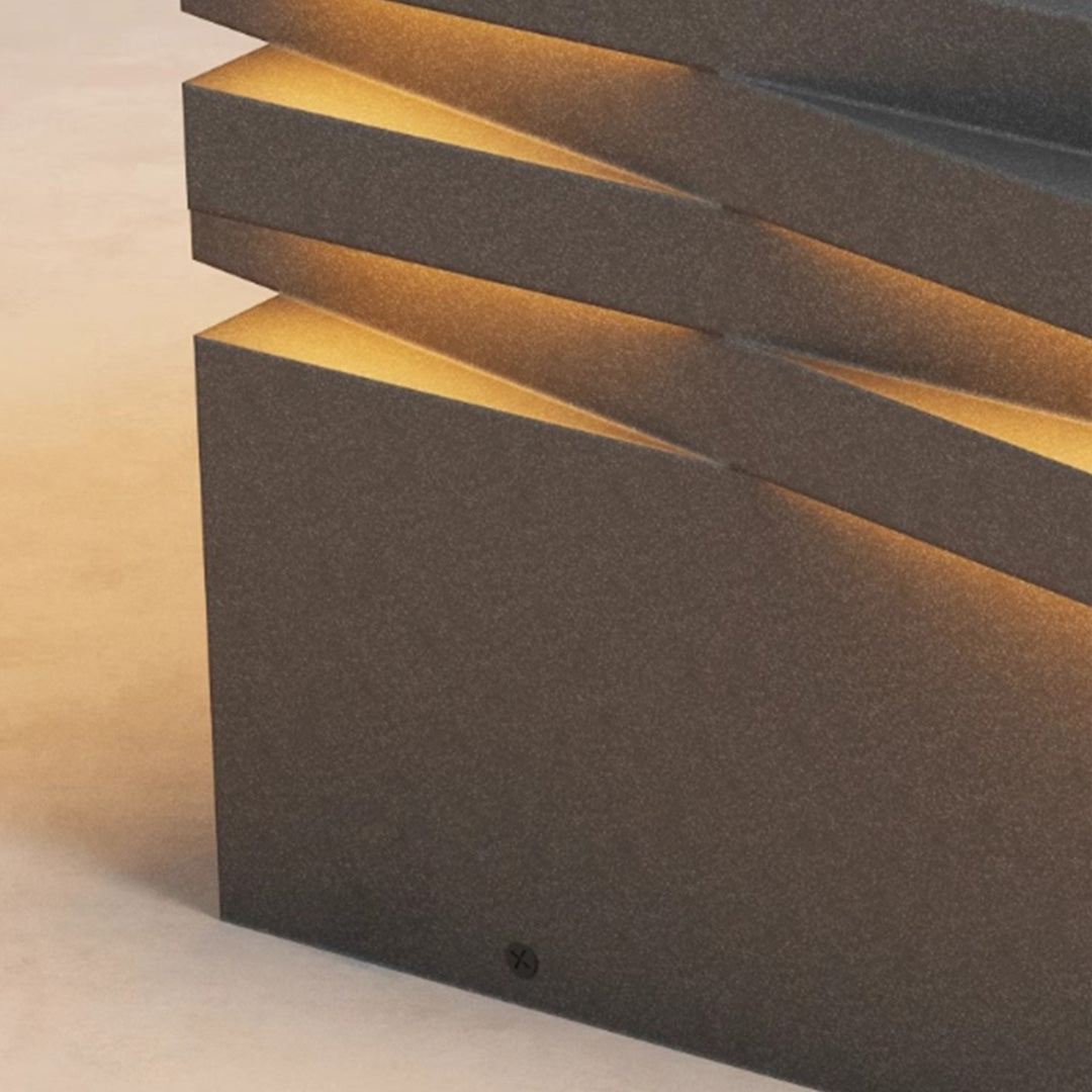 Close-up detail of gate post solar pillar light showing textured layered metal frame and warm glow.