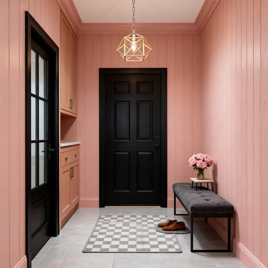 Single geometric gold metal pendant light illuminating a modern mudroom with pink paneling and a black door for contrast.