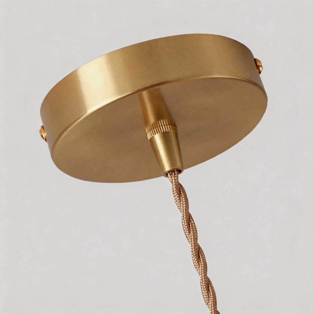 Close-up of the round brass canopy and twisted cord on a geometric pendant light.