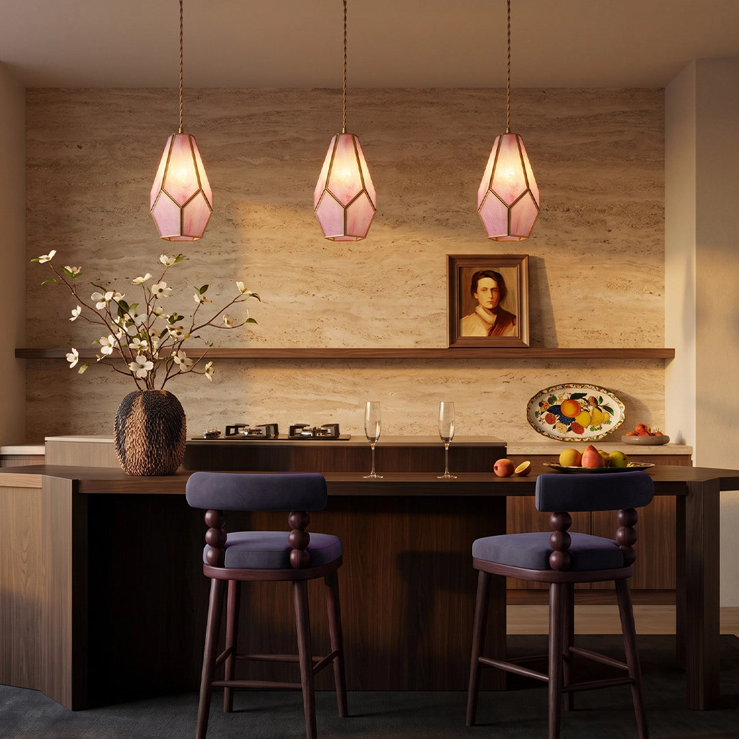 Pink geometric pendant lights hanging above a kitchen island in a warm neutral kitchen.