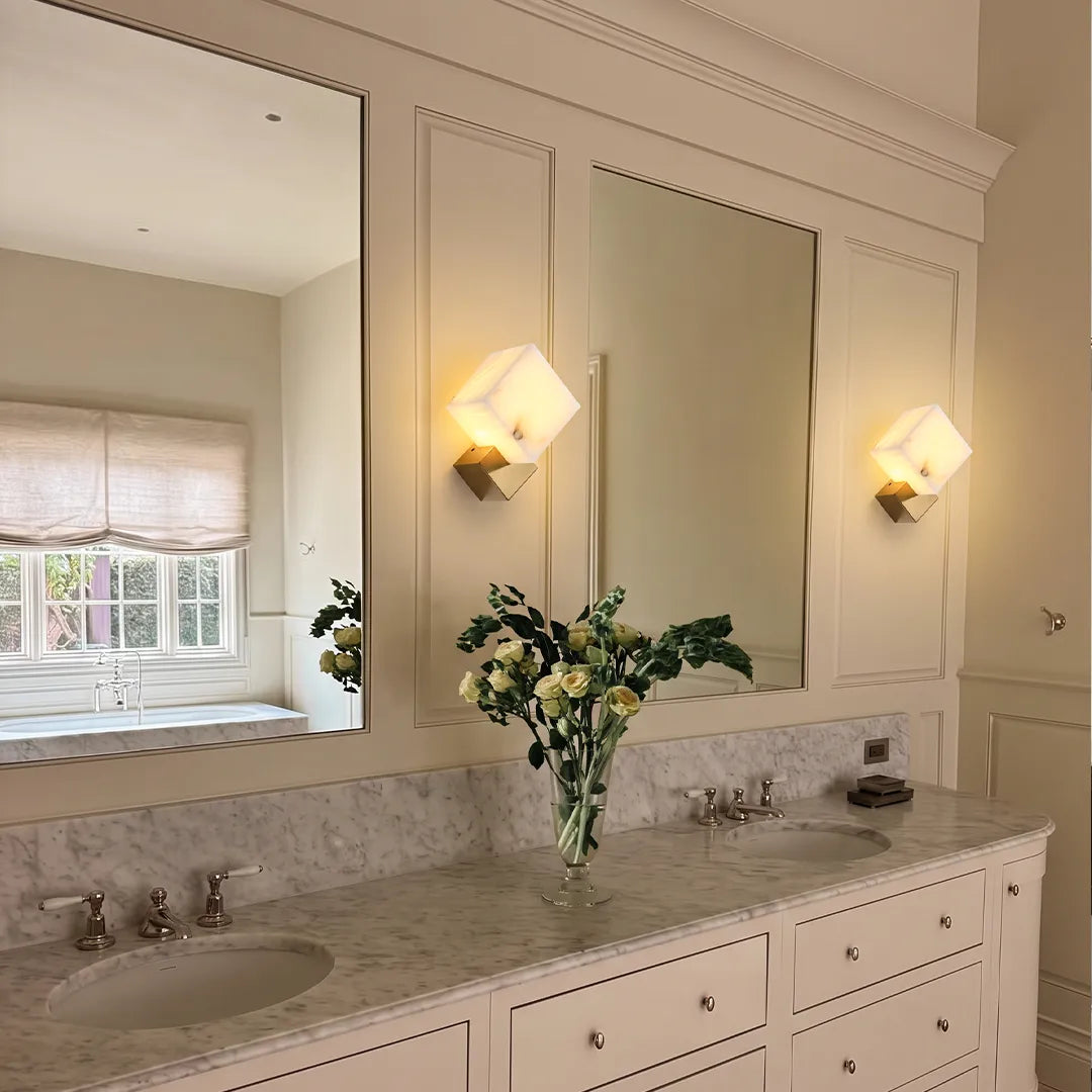 Geometric wall sconces installed beside a bathroom mirror above a marble vanity.