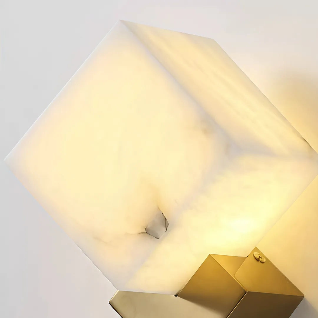 Close-up of a geometric wall sconce with a glowing stone cube shade and gold base.