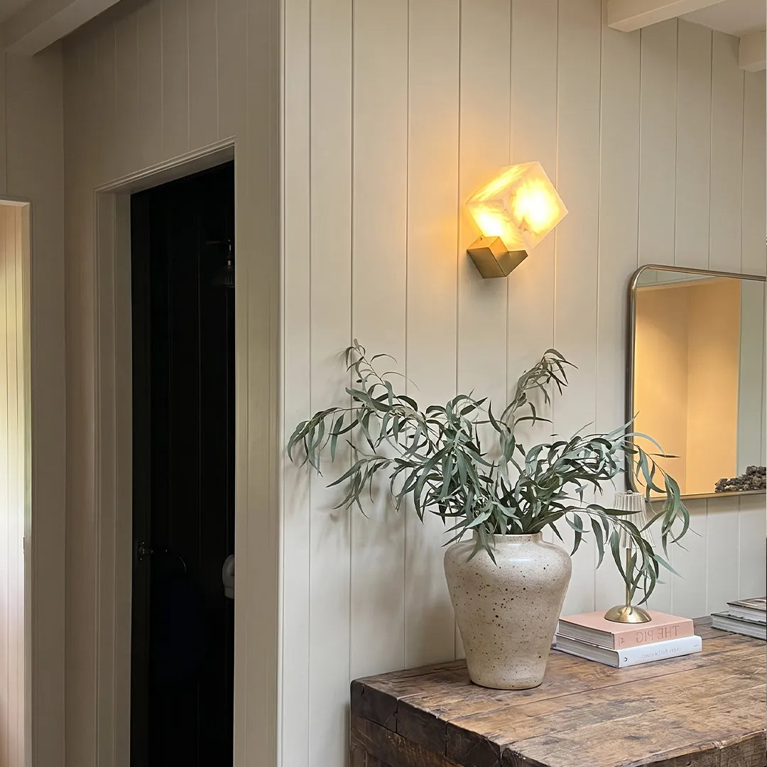 Geometric wall sconce illuminating a hallway corner above a stone console table.