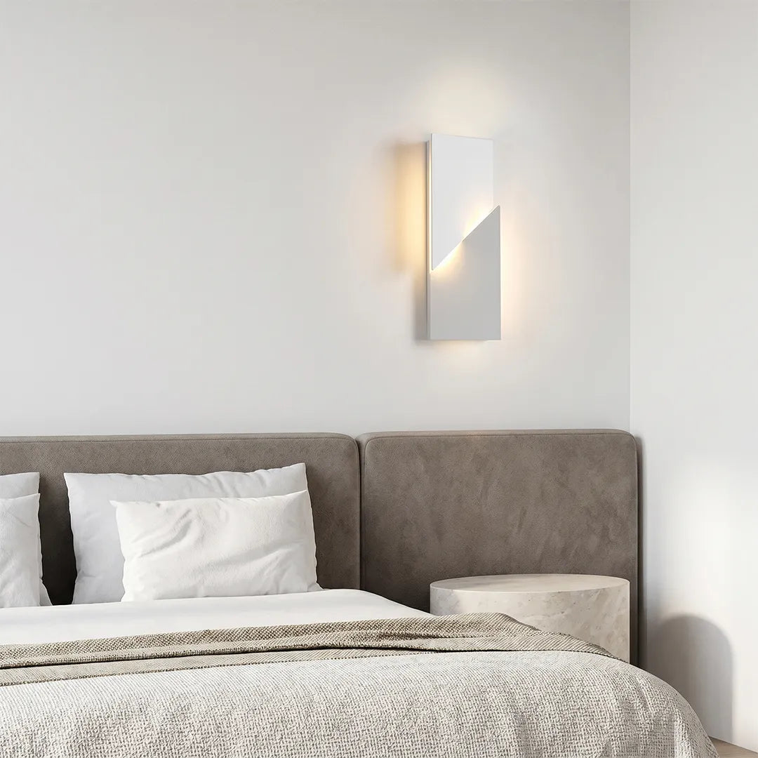 Geometric wall sconce light installed beside a bed, adding soft ambient illumination to a neutral bedroom wall.