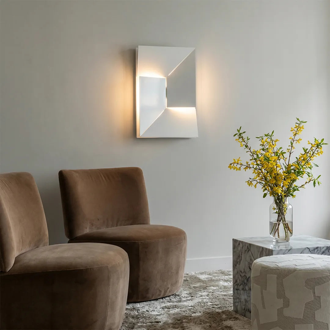 Geometric wall sconce light in a modern living room, featuring an illuminated faceted design above two accent chairs.