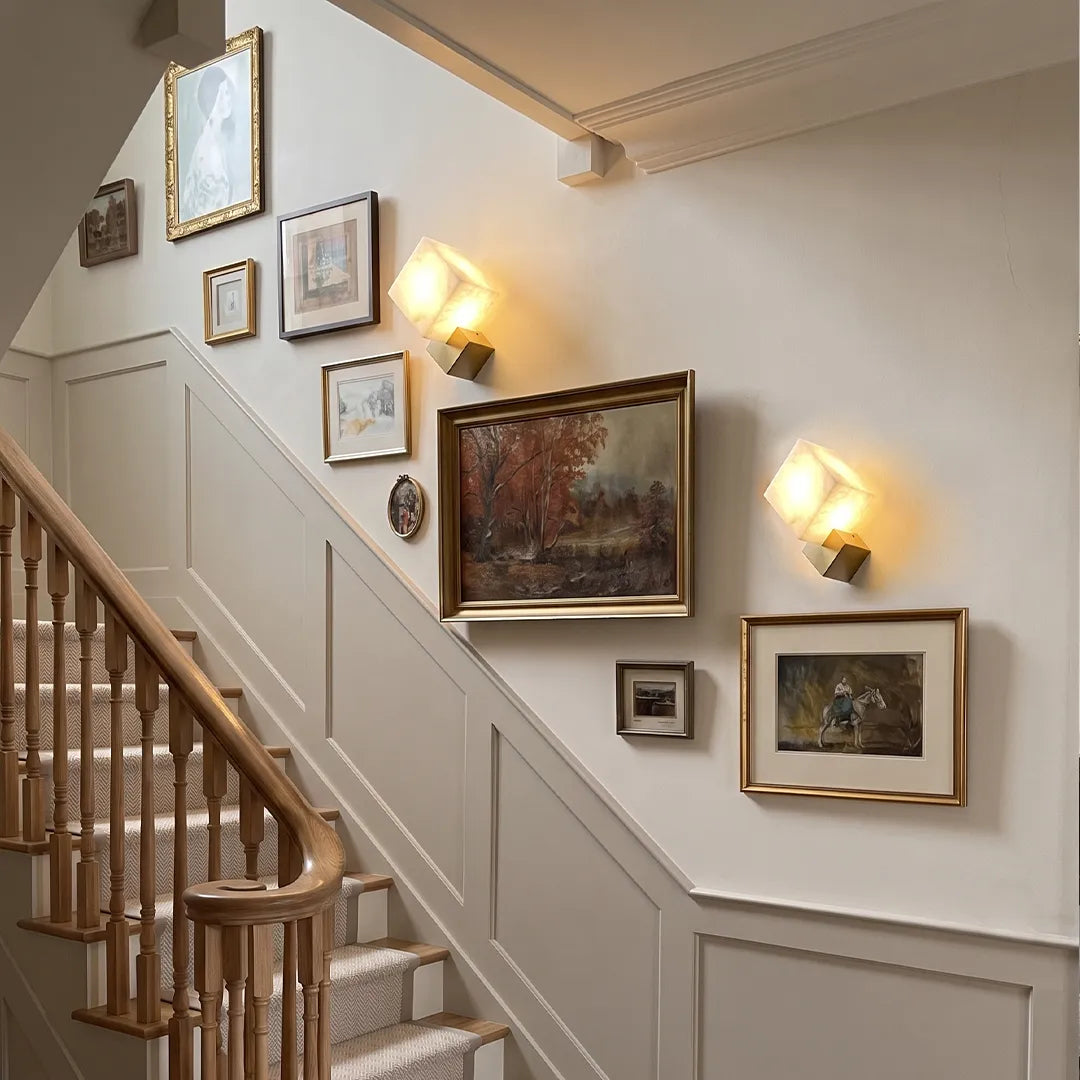 Geometric wall sconces displayed along a staircase gallery wall with framed artwork.