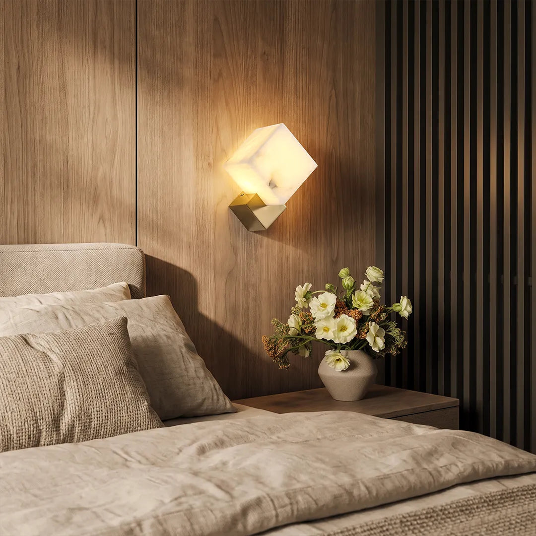 Geometric wall sconce mounted on a wood-paneled wall above a bedside table.