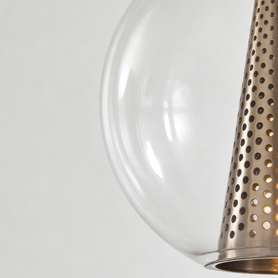 Clear glass ball pendant lights with a smooth transparent globe paired with a perforated metal shade detail in a modern lighting design.