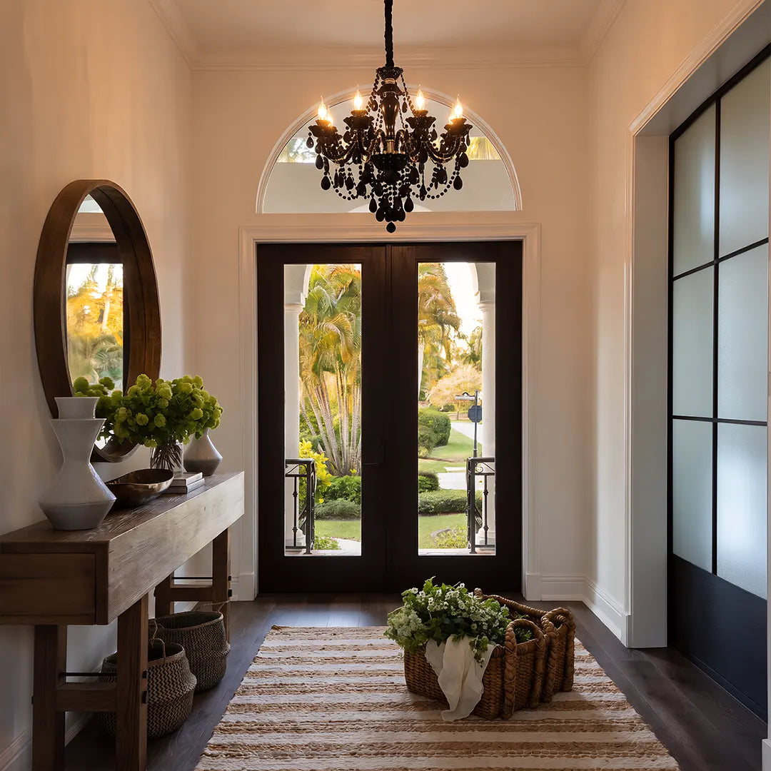 Glass candlelight chandelier hanging in an elegant entryway with an arched glass door and console table.