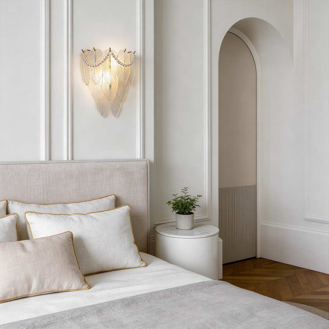 Glass feather wall light mounted above a bed with white pillows and a minimalist decor.