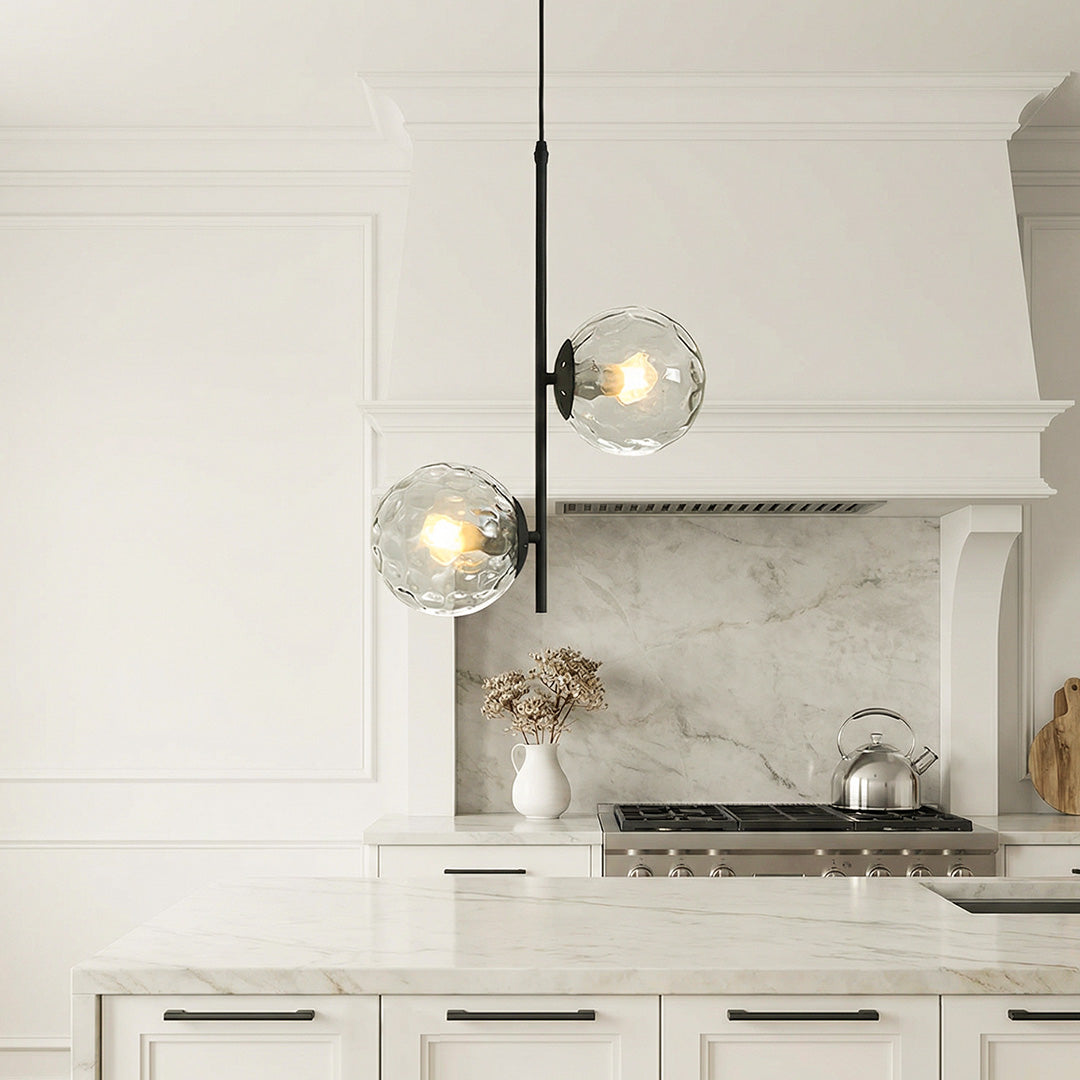 Sleek glass hanging pendant lights with water-ripple globes hanging over a luxury white island.
