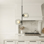 Sleek glass hanging pendant lights with water-ripple globes hanging over a luxury white island.