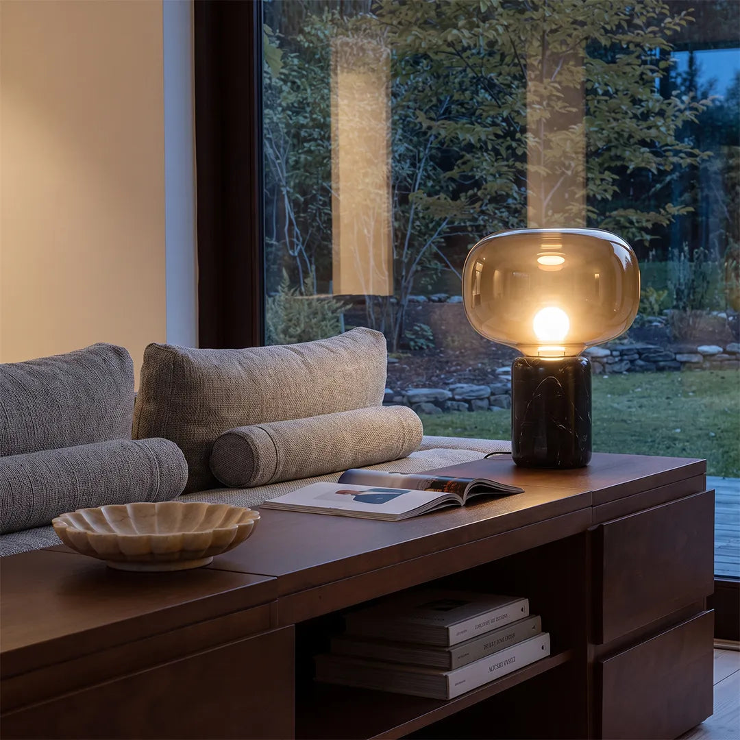 Glass modern table lamps displayed on a dark wood console table beside a large window in a contemporary interior.