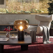 Glass modern table lamps placed on a low coffee table in a cozy living room with a lounge chair and large window.
