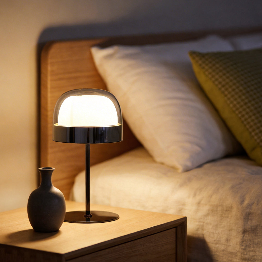 Glass mushroom table lamp with a black base, placed on a nightstand beside a bed.