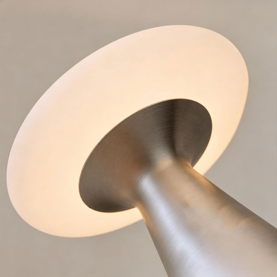 Close-up of a glass mushroom table lamp showing the glowing mushroom shade and metallic cone base.