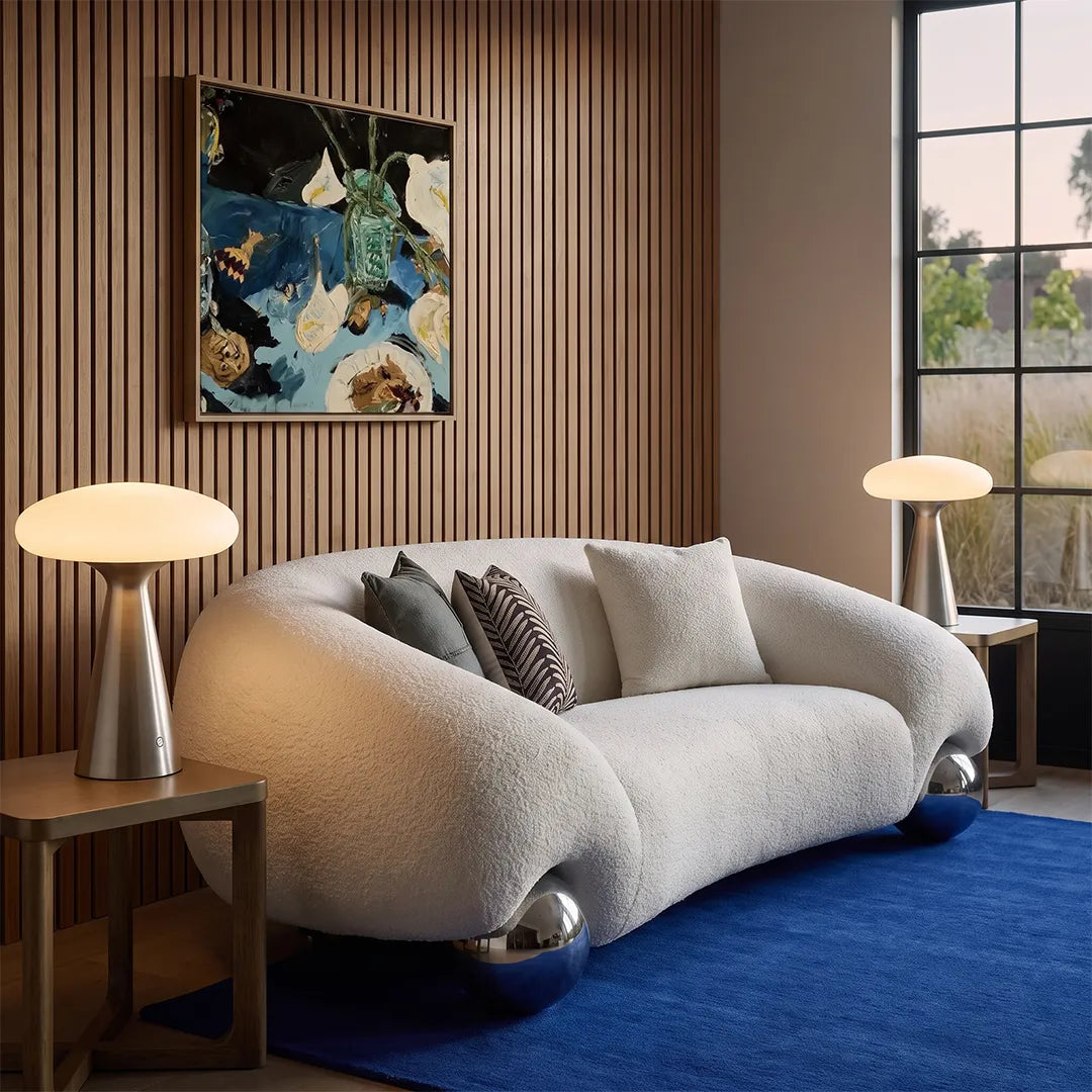 Glass mushroom table lamps styled on side tables beside a curved sofa in a contemporary lounge with wood paneling.