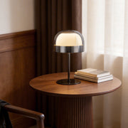 Glass mushroom table lamp with a sleek design on a wooden side table in a modern bedroom.