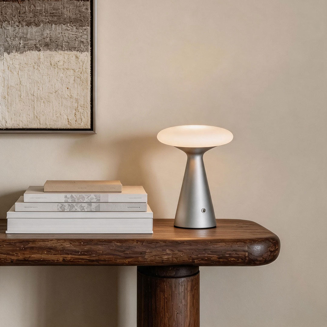 Glass mushroom table lamp styled on a wooden side table with stacked books in a soft neutral interior.